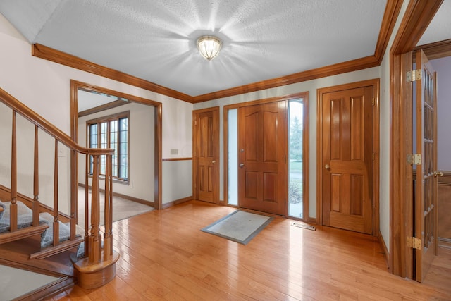 foyer entrance with light wood-type flooring, a textured ceiling, and ornamental molding