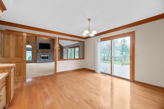 unfurnished living room with crown molding, a fireplace, light wood-type flooring, and a notable chandelier