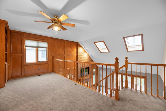 bonus room featuring light carpet, lofted ceiling with skylight, ceiling fan, and wooden walls