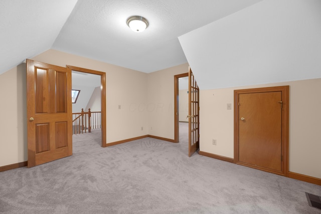 bonus room with a textured ceiling, light colored carpet, and lofted ceiling