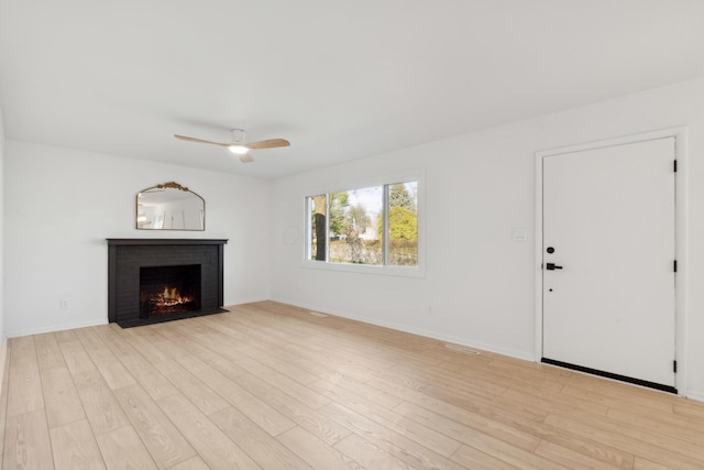 unfurnished living room featuring a brick fireplace, ceiling fan, and light hardwood / wood-style flooring