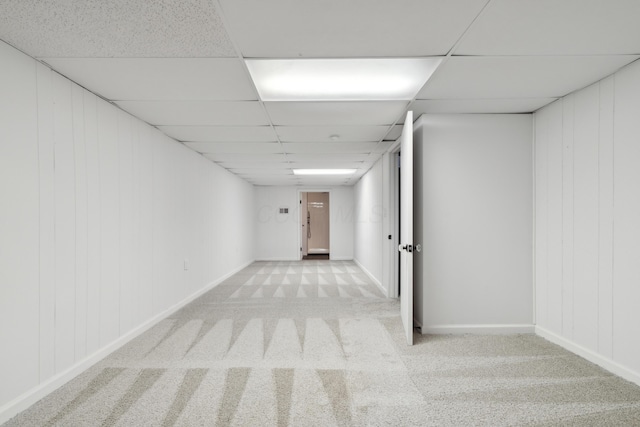 basement with light carpet, a drop ceiling, and wooden walls