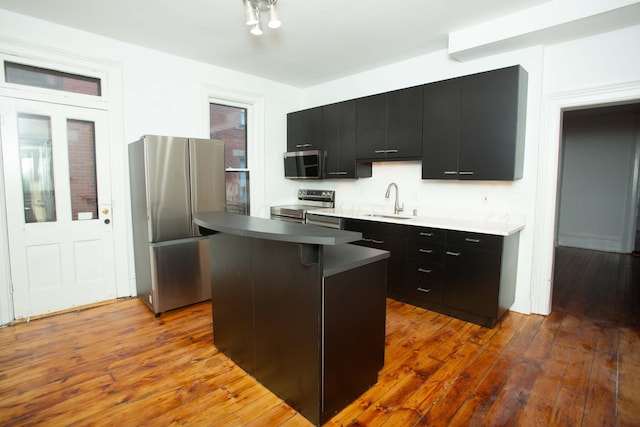 kitchen featuring sink, hardwood / wood-style floors, a kitchen bar, a kitchen island, and appliances with stainless steel finishes