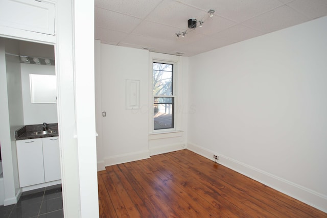 empty room with dark hardwood / wood-style floors, a drop ceiling, and sink