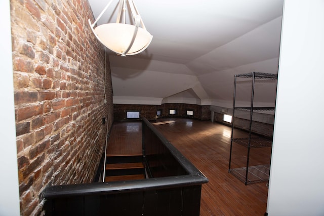 stairway featuring hardwood / wood-style flooring, lofted ceiling, and brick wall