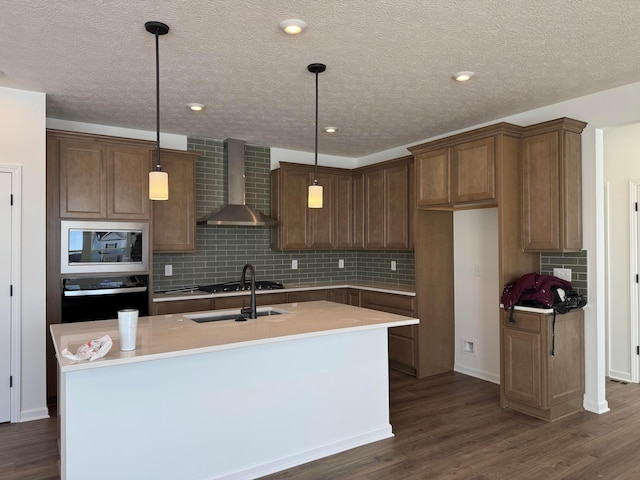 kitchen featuring a center island with sink, oven, wall chimney exhaust hood, and decorative light fixtures