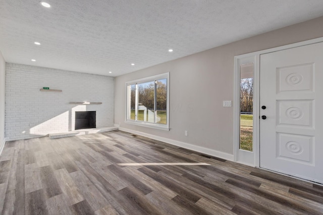 unfurnished living room featuring a fireplace, dark hardwood / wood-style floors, a textured ceiling, and brick wall