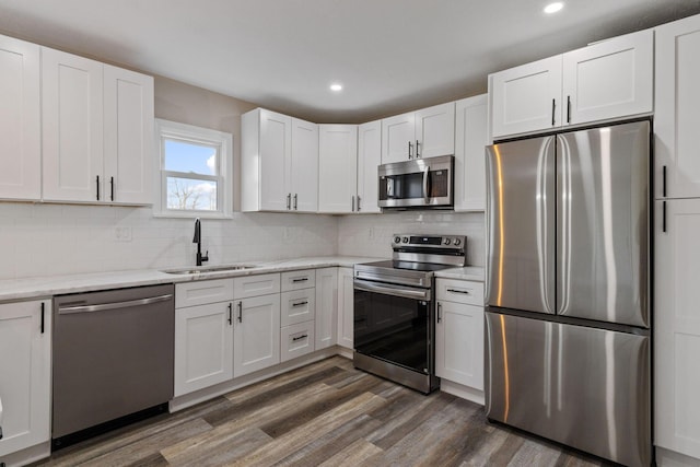 kitchen featuring appliances with stainless steel finishes, sink, white cabinets, light stone countertops, and dark wood-type flooring