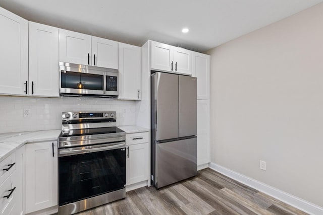 kitchen with stainless steel appliances, tasteful backsplash, wood-type flooring, light stone countertops, and white cabinets