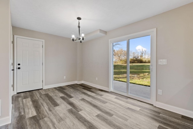 empty room featuring wood-type flooring and an inviting chandelier