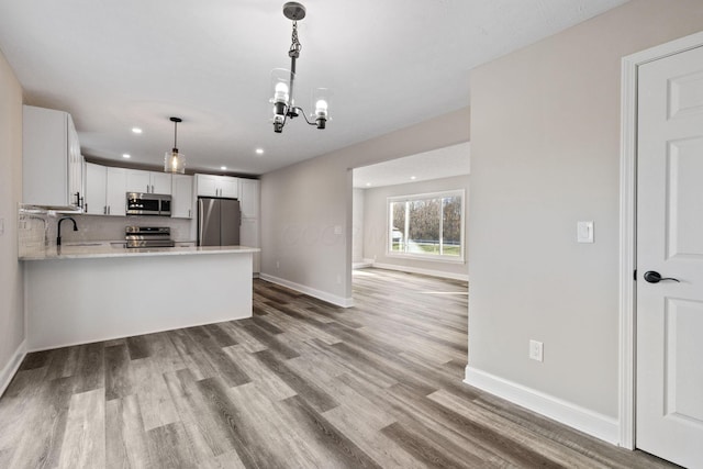 kitchen featuring hanging light fixtures, stainless steel appliances, light hardwood / wood-style floors, white cabinets, and kitchen peninsula