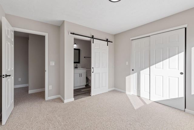 unfurnished bedroom featuring sink, connected bathroom, a barn door, light colored carpet, and a closet