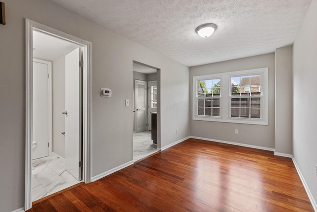 unfurnished bedroom with hardwood / wood-style floors, ensuite bath, and a textured ceiling