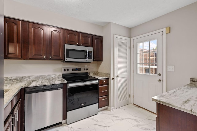 kitchen with light stone counters, stainless steel appliances, dark brown cabinets, and a textured ceiling