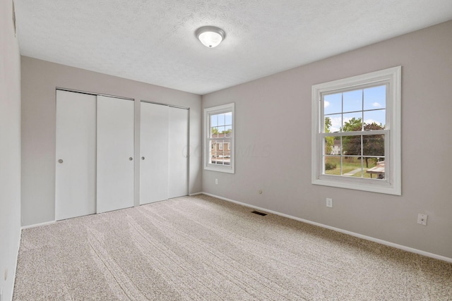 unfurnished bedroom featuring a textured ceiling, multiple closets, and carpet flooring