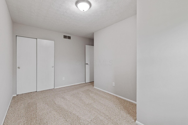 unfurnished bedroom featuring light colored carpet, a textured ceiling, and a closet