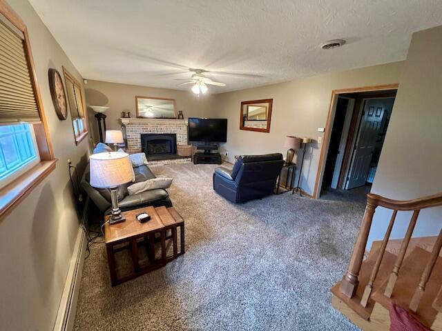 living room featuring carpet flooring, a textured ceiling, ceiling fan, a baseboard heating unit, and a fireplace