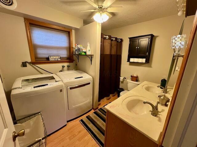 clothes washing area featuring ceiling fan, sink, light hardwood / wood-style flooring, a textured ceiling, and washer and clothes dryer