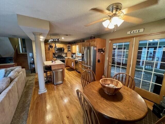 dining room featuring ceiling fan, ornate columns, a textured ceiling, and light hardwood / wood-style flooring