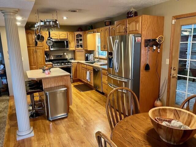 kitchen featuring a center island, sink, light hardwood / wood-style flooring, ornate columns, and stainless steel appliances