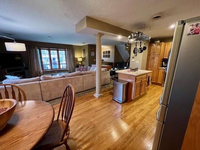 kitchen with stainless steel refrigerator, ornate columns, a textured ceiling, a kitchen island, and light wood-type flooring