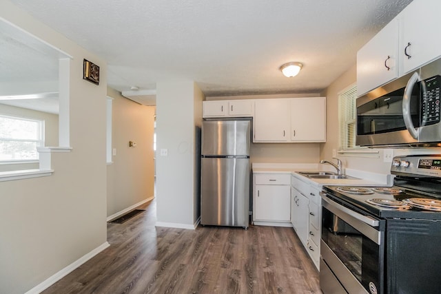 kitchen featuring baseboards, dark wood-style floors, appliances with stainless steel finishes, white cabinetry, and a sink