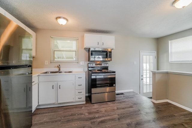 kitchen featuring dark wood-style floors, stainless steel appliances, visible vents, white cabinetry, and a sink