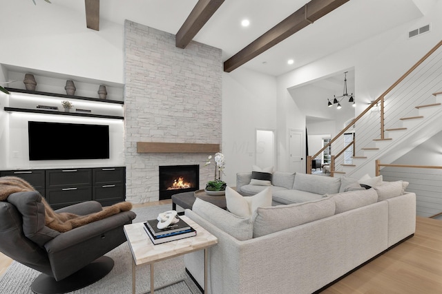 living room with beam ceiling, light hardwood / wood-style floors, a stone fireplace, and a towering ceiling