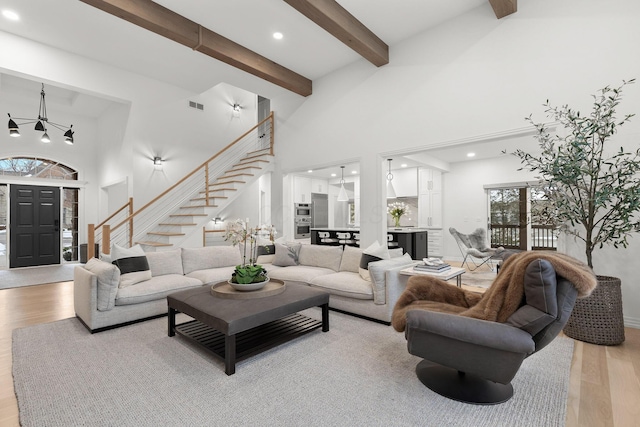 living room with a high ceiling, a chandelier, light wood-type flooring, and beamed ceiling