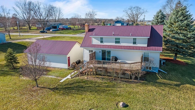 back of property featuring a chimney, a yard, an outbuilding, metal roof, and a wooden deck