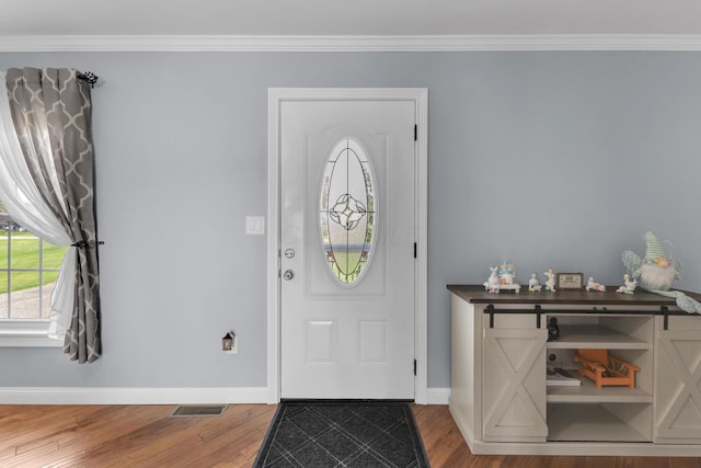 foyer featuring ornamental molding, visible vents, wood finished floors, and baseboards