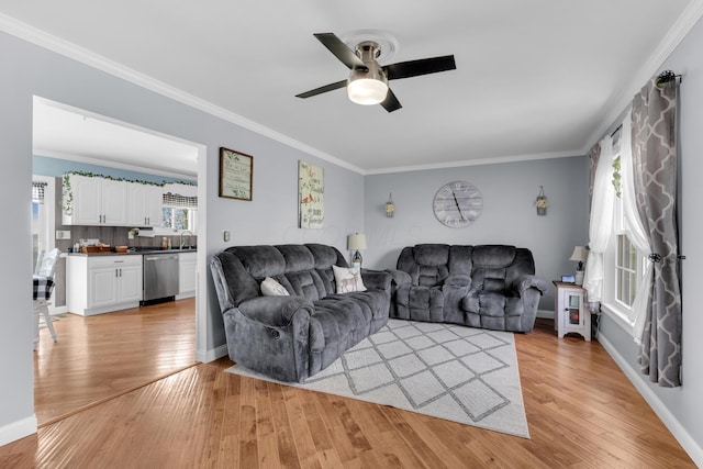 living area with baseboards, ornamental molding, ceiling fan, and light wood-style floors