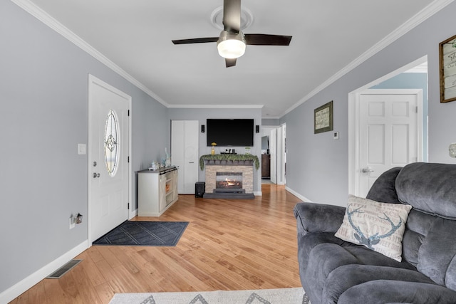 living area with crown molding, visible vents, light wood finished floors, a fireplace, and a ceiling fan