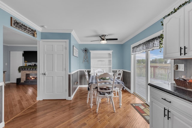 dining space featuring ceiling fan, crown molding, light wood-style flooring, and wainscoting