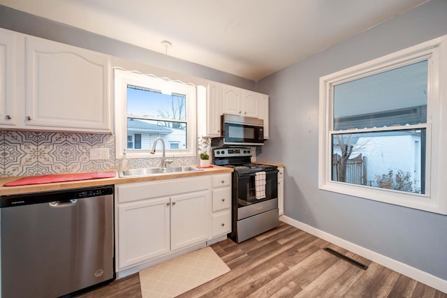 kitchen featuring sink, backsplash, decorative light fixtures, white cabinets, and appliances with stainless steel finishes