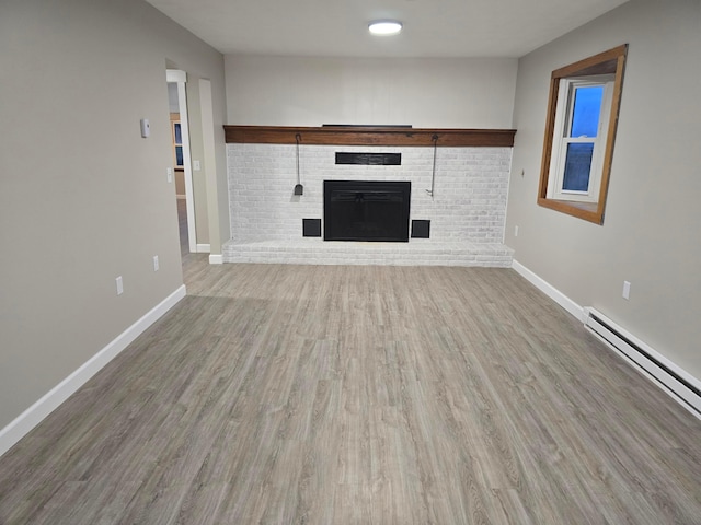 unfurnished living room with hardwood / wood-style flooring, a baseboard heating unit, and a brick fireplace