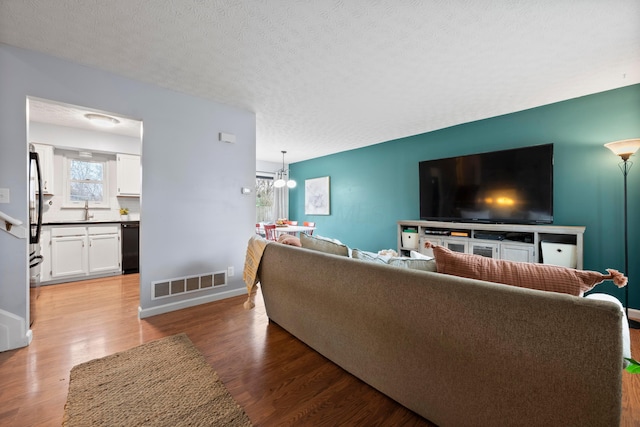 living room featuring a textured ceiling, a chandelier, hardwood / wood-style flooring, and sink