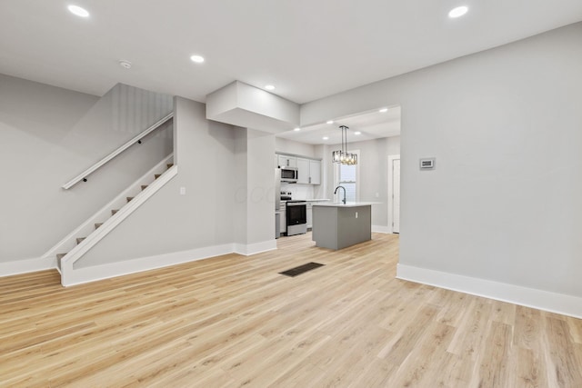 unfurnished living room with light hardwood / wood-style floors, sink, and an inviting chandelier