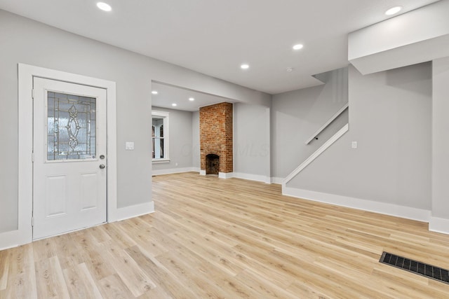 unfurnished living room featuring light hardwood / wood-style floors and a brick fireplace