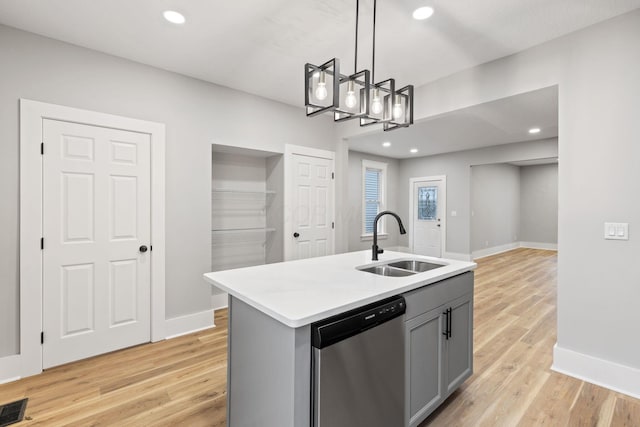 kitchen with stainless steel dishwasher, decorative light fixtures, a center island with sink, light hardwood / wood-style flooring, and gray cabinets