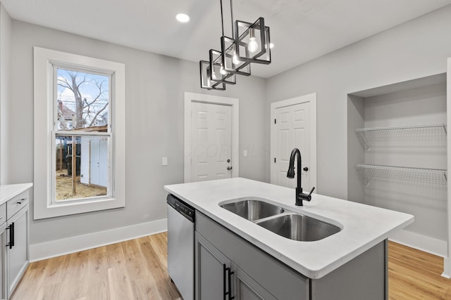 kitchen with gray cabinetry, a center island with sink, sink, stainless steel dishwasher, and decorative light fixtures