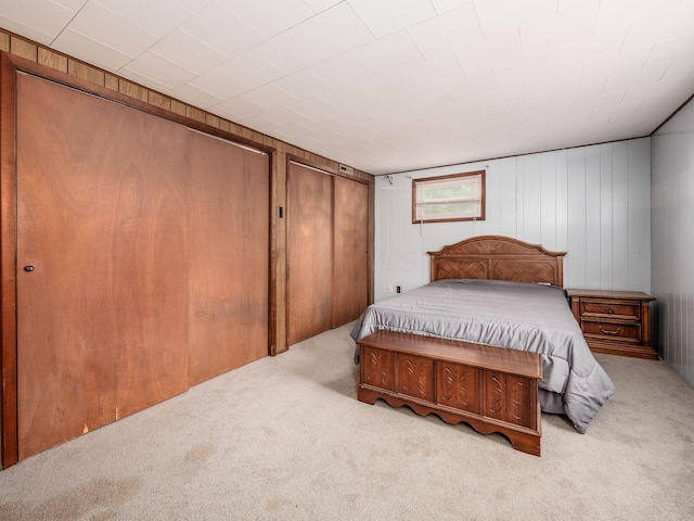 bedroom featuring wooden walls, light colored carpet, and multiple closets