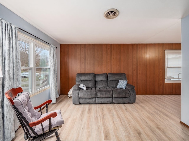 living room featuring plenty of natural light, light wood-type flooring, and wood walls