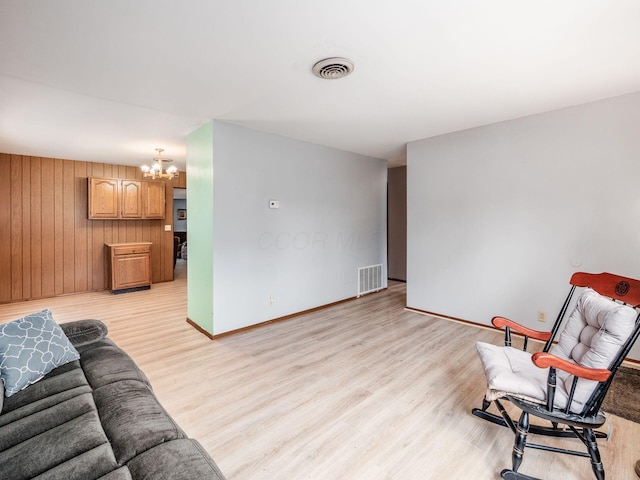 living room featuring wooden walls, light hardwood / wood-style floors, and a chandelier