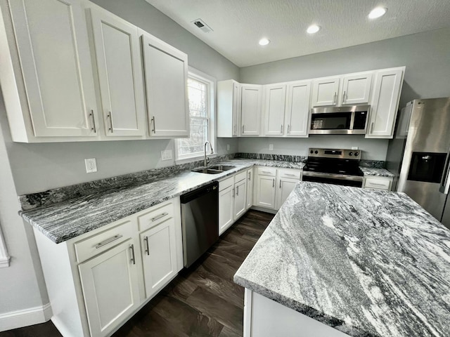 kitchen featuring light stone counters, a textured ceiling, stainless steel appliances, sink, and white cabinetry