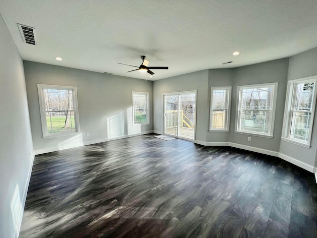 empty room with ceiling fan, plenty of natural light, dark wood-type flooring, and a textured ceiling