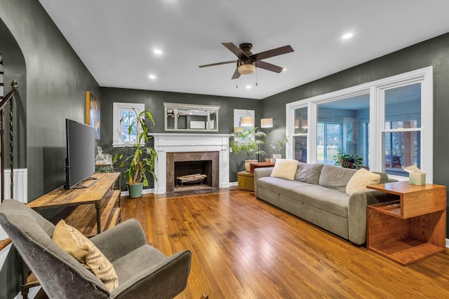 living room with hardwood / wood-style flooring, ceiling fan, and a tiled fireplace