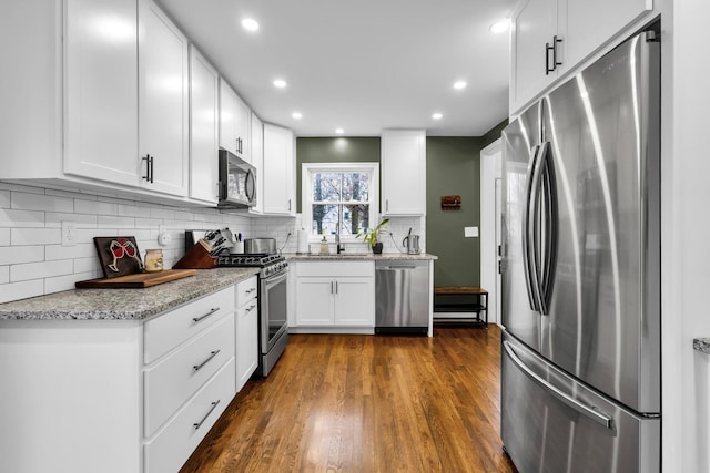 kitchen featuring light stone countertops, sink, dark wood-type flooring, stainless steel appliances, and white cabinets