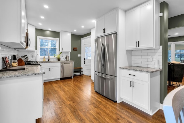 kitchen with dark wood-type flooring, decorative backsplash, light stone countertops, appliances with stainless steel finishes, and white cabinetry