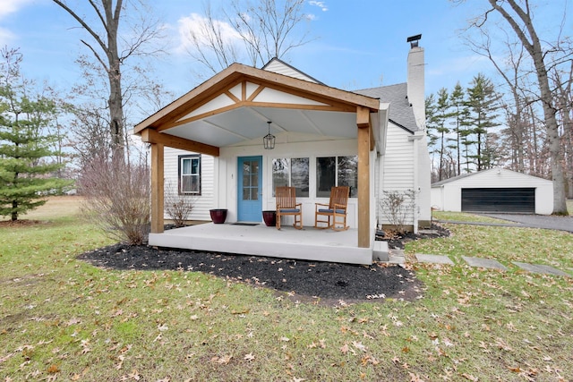 rear view of property featuring a yard, covered porch, an outdoor structure, and a garage